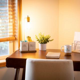 A cozy home office setup with a desk lamp, notebook, mug, and potted plant by the window.