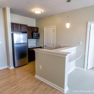 A modern kitchen area in an apartment with hardwood floors and stainless steel appliances.