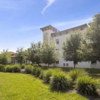 A scenic view of a building surrounded by trees and a well-maintained grassy area on a sunny day.