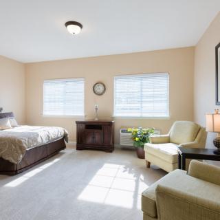 A bright and cozy bedroom with a bed, chairs, and ample natural light streaming through the windows.
