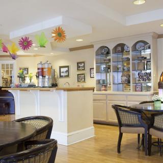 A cozy cafe interior with tables and chairs, colorful decorations, beverage dispensers, and wooden flooring.