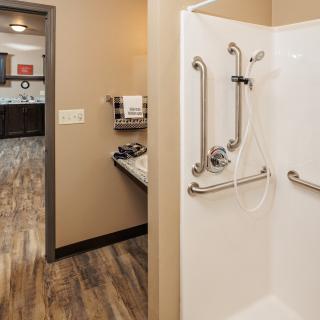 A modern, accessible hotel bathroom with a walk-in shower and grab bars.