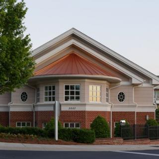 A suburban building with a mix of brick and siding, featuring large windows and surrounded by greenery.