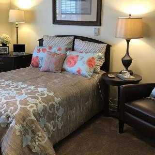 A cozy bedroom with a neatly made bed featuring floral pillows, two lamps on nightstands, and a comfortable chair.