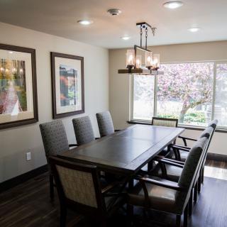 A well-lit dining room featuring a large table and six chairs, complemented by artwork and a chandelier.