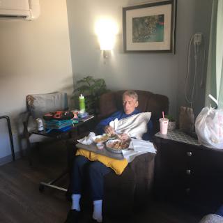 An elderly person relaxing in a living room, surrounded by food and beverages.