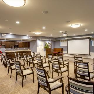 A well-lit conference room equipped with arranged chairs and a projector screen for presentations.