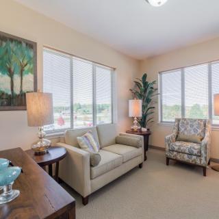 A cozy living room with a sofa, armchair, and soft lighting from lamps near large windows.