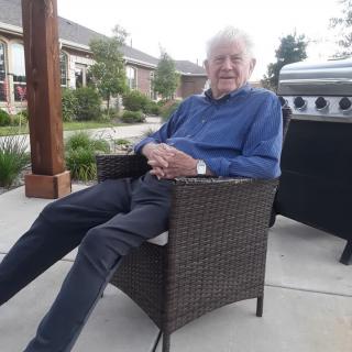 An elderly man is relaxing on a patio chair outdoors.