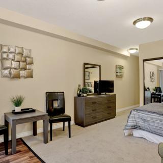A modern bedroom with a neatly arranged interior, featuring a bed, dresser with mirror, TV, and decorative elements.