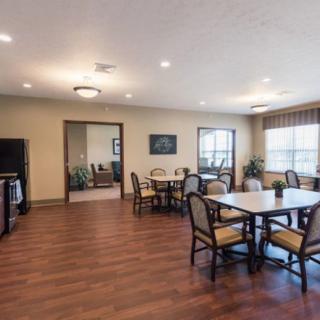 A spacious dining area with wooden flooring, tables, and chairs, well-lit by ceiling lights and natural light from large windows.