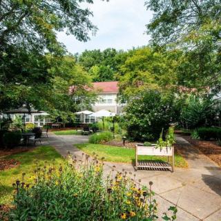 A scenic garden pathway leading to a quaint building, surrounded by lush greenery and comfortable benches.