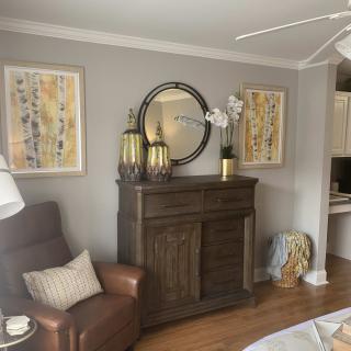 A cozy living room with elegant decor, featuring a dark wooden cabinet topped with decorative items and framed artwork on the walls.