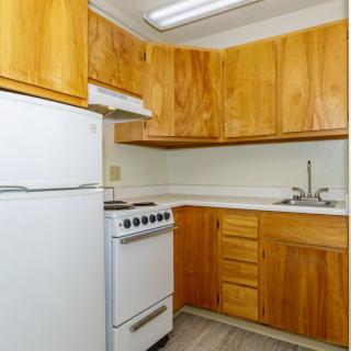 A compact kitchen with wooden cabinets, featuring a refrigerator, stove, and sink.