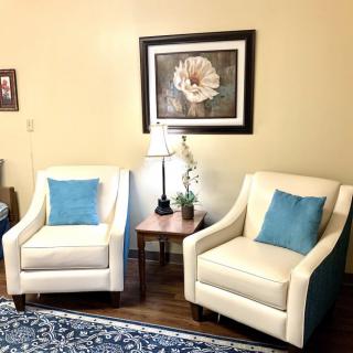A cozy living room setup featuring two cream armchairs with blue cushions, accompanied by a lamp and wall art.