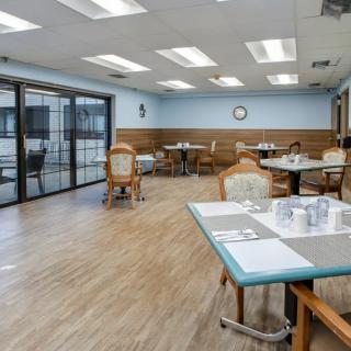 A spacious dining area with neatly arranged tables and chairs, featuring a wooden floor and bright overhead lighting.