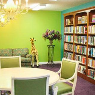 A cozy library room with a green accent wall, bookshelves, a chandelier, and comfortable seating.