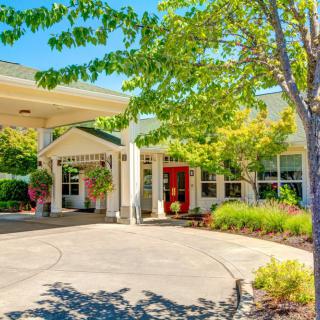 A sunny view of a building entrance surrounded by lush greenery and landscaping.