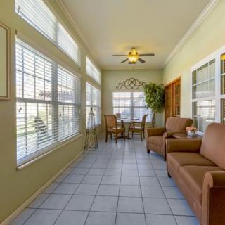 A cozy sunroom with comfortable seating, large windows with blinds, and a small dining table under a ceiling fan.