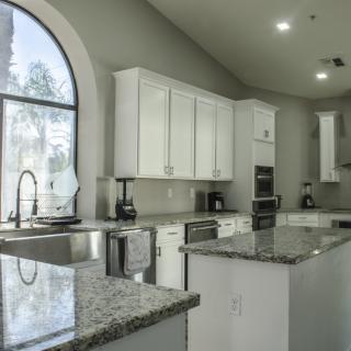 A modern kitchen with white cabinets, granite countertops, and a large window providing natural light.