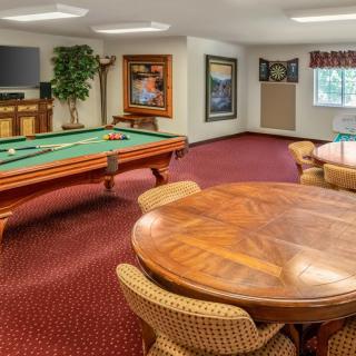 A spacious recreation room featuring a billiards table, seating area with a large round wooden table, and artwork on the walls.