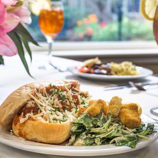 A delicious sandwich served with salad and fried sides on a neatly arranged dining table, accompanied by a refreshing drink.