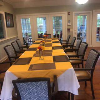 A dining room with a long table covered in yellow tablecloths, set with chairs and simple centerpieces.