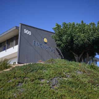 A modern building with a company logo on its exterior wall, surrounded by greenery and under a clear blue sky.