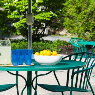 A patio setup with a green table and chairs, featuring a pitcher of lemonade and a bowl of lemons.