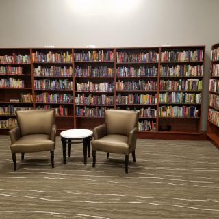 A cozy reading area with two chairs and a small table in front of bookshelves filled with books.