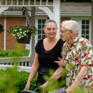 A caregiver and an elderly person enjoy a conversation in a beautifully landscaped garden.