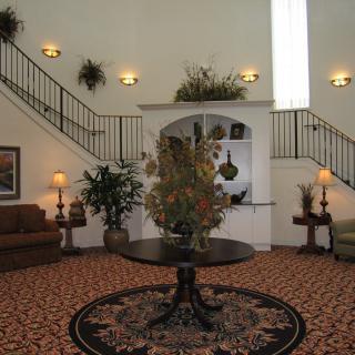 A spacious and elegantly decorated lobby with a round table centerpiece, surrounded by comfortable seating and greenery.