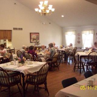 A cozy dining room with people sitting at tables, enjoying a meal under a chandelier.