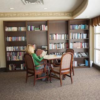 A woman reading at a table in a library with bookshelves in the background.