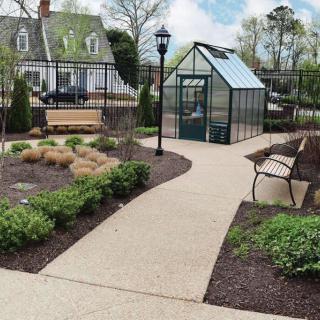 A peaceful garden scene with a greenhouse, a winding pathway, and a bench for relaxation.