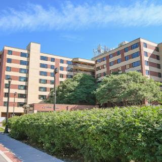 A modern hospital building surrounded by greenery under a clear blue sky.