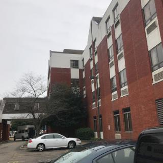 A view of a brick hotel building with a parking area under a cloudy sky.