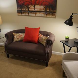 Cozy living room setup with a brown sofa, red and floral cushions, stylish lamps, and wall art.