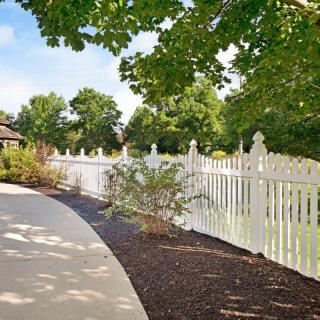 A serene garden pathway bordered by a white picket fence and lush greenery.
