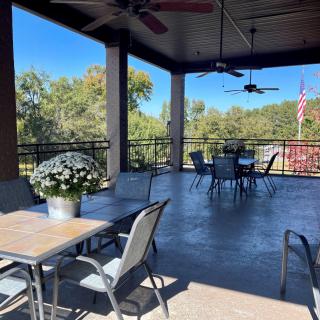 A spacious outdoor patio with tables, chairs, and ceiling fans, offering a scenic view.