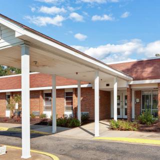 The image shows a one-story building with a brick facade featuring a covered entrance and a clear sky in the background.