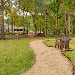 A serene park scene with a winding pathway and a wooden bench surrounded by trees.