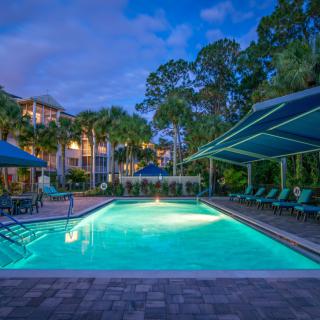 A serene resort swimming pool area illuminated at dusk, surrounded by trees and lounge chairs.