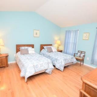 A cozy bedroom with twin beds and light blue walls, featuring hardwood floors and soft lighting from decorative lamps.