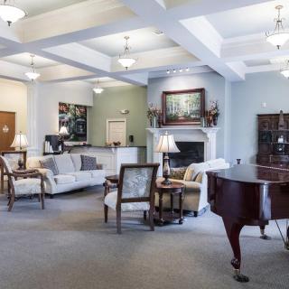 A spacious and elegantly decorated living room featuring a grand piano, comfortable sofas, and a cozy fireplace.