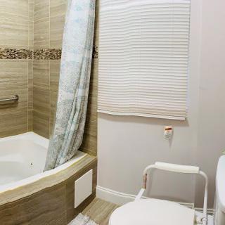 A bathroom with a bathtub, toilet, and accessibility chair.