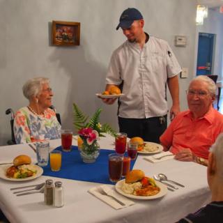 A waiter serves a meal to elderly patrons at a restaurant table.