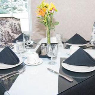 A neatly set dining table with black napkins, glassware, and a flower vase centerpiece.