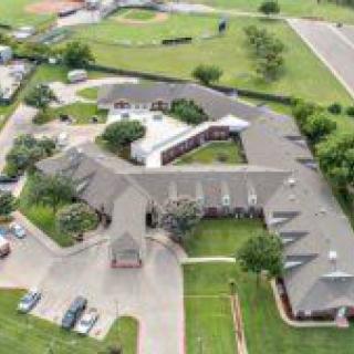 Aerial view of a large building complex surrounded by green fields and parking areas.