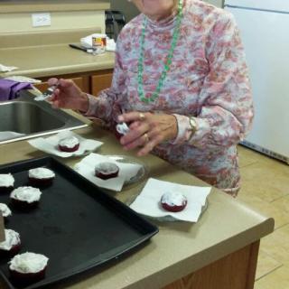 An elderly woman is frosting cupcakes in a kitchen.